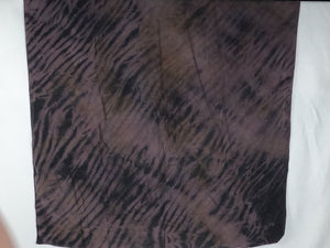 A silk square shawl laid flat. It is light mauve and dark brown in colour. It has a ripple like print.