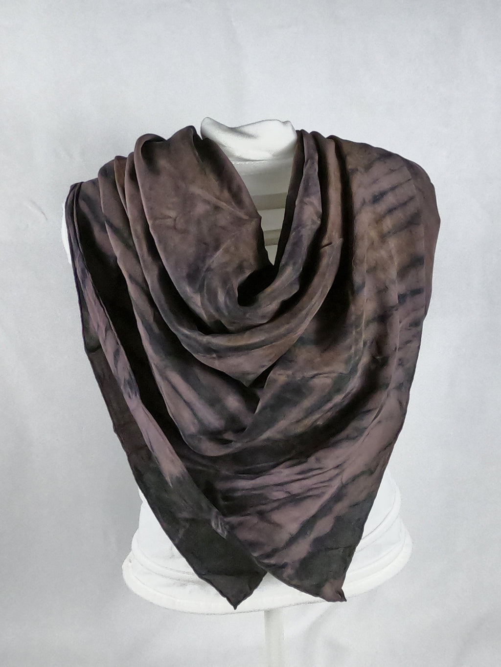 A silk square shawl styled on a mannequin. It is light mauve and dark brown in colour. It has a ripple like print.