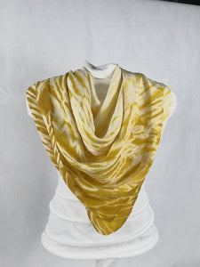A silk square shawl styled on a mannequin. It is dark yellow in colour with a ripple like print.