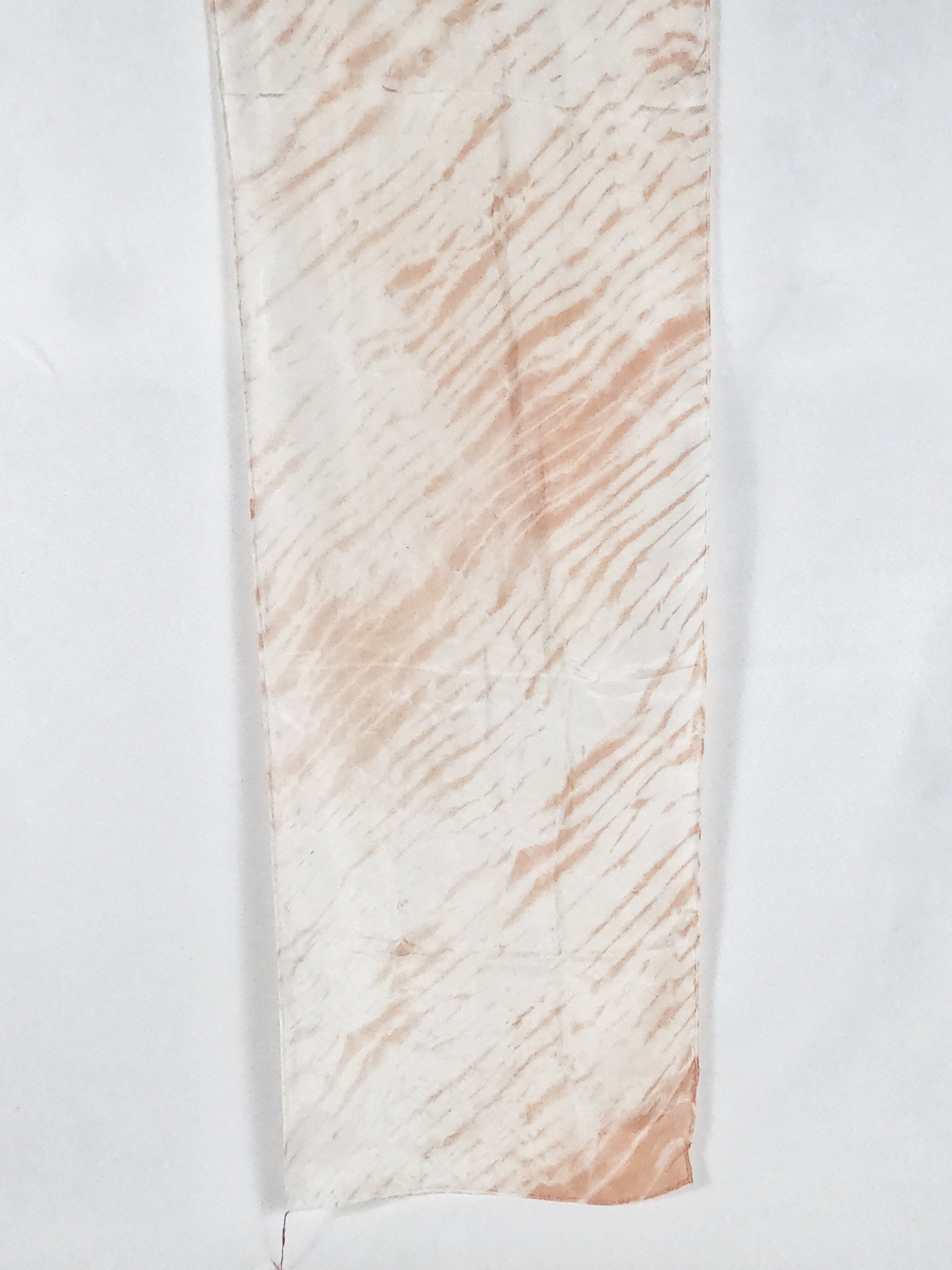 A silk scarf laid flat. It is white and peach in colour. It has a ripple like print.